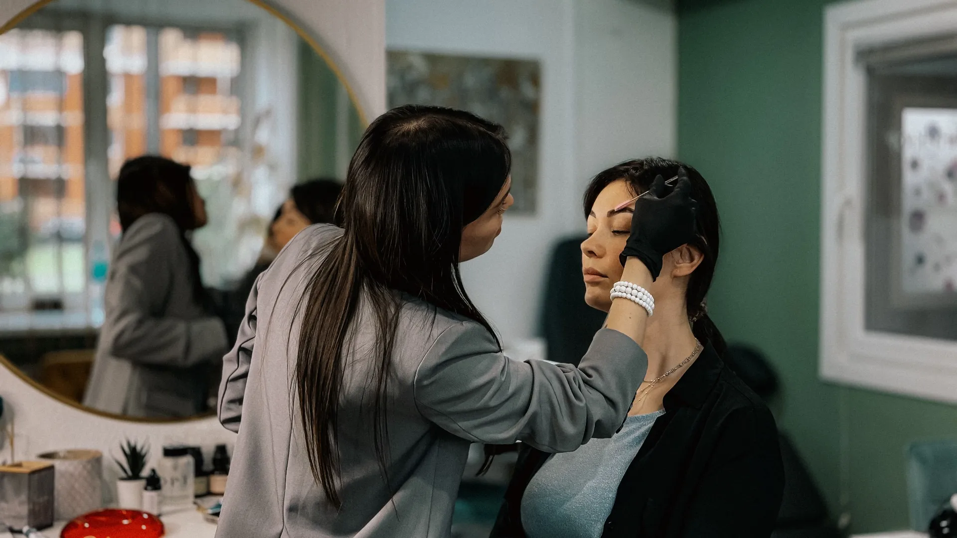 Brow artist shapes a relaxed client's eyebrows at a salon mirror — a quick, customized brow service, never a template.