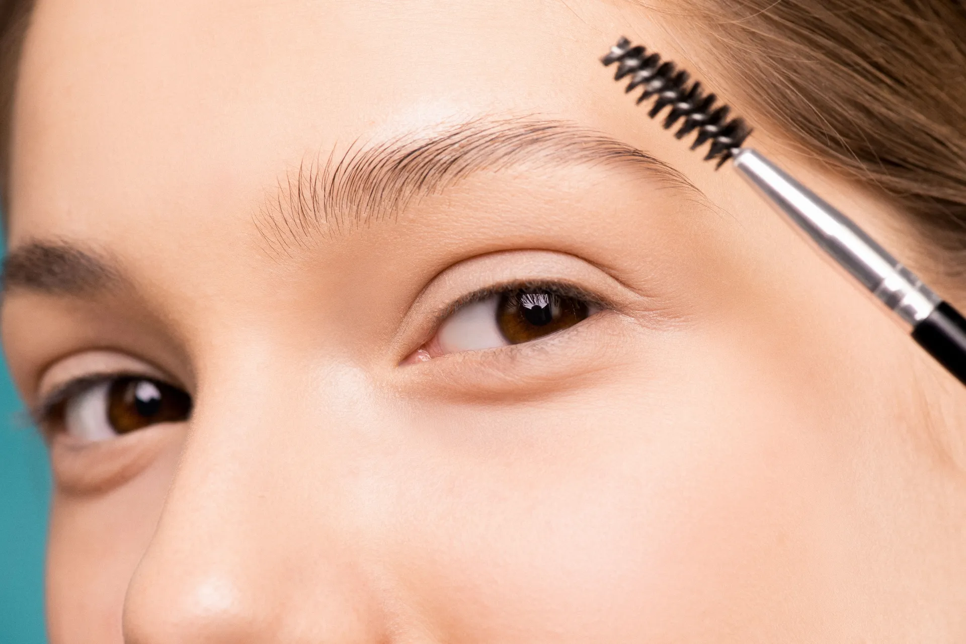 Spoolie brush lifting and combing a full eyebrow upward into the smooth, sculpted shape created by brow lamination.